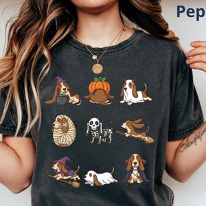 Pu&ograve; includere: Una t-shirt grigio antracite con una stampa grafica di nove Basset Hound in vari costumi di Halloween, tra cui una strega, una zucca, un diavolo, una mummia, uno scheletro e un vampiro. Il testo Pepper &egrave; stampato in alto a destra.