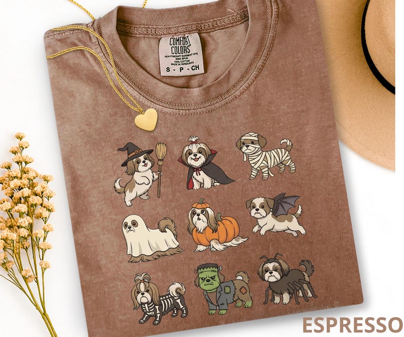 Op de afbeelding: Een bruin t-shirt met een grafische print van negen Shih Tzu honden in verschillende Halloween-kostuums, waaronder een heks, vampier, mummie, spook, pompoen, vleermuis, skelet, het monster van Frankenstein en een spin.