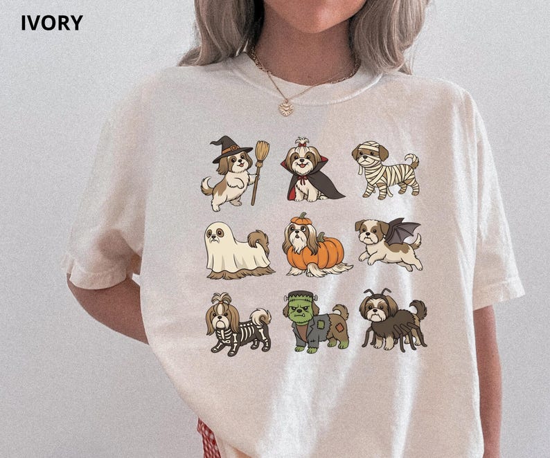 Op de afbeelding: Een ivoorkleurig t-shirt met een grafische print van negen Shih Tzu honden in verschillende Halloween-kostuums, waaronder een heks, vampier, mummie, spook, pompoen, vleermuis, skelet, Frankenstein's monster en een spin, gerangschikt in een raster.