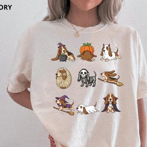 Pu&ograve; includere: Una t-shirt color avorio con una stampa grafica di nove basset hound in vari costumi di Halloween, tra cui una strega, una zucca, un fantasma, una mummia, uno scheletro, un cavaliere su scopa e un vampiro, con la parola IVORY stampata nell'angolo.