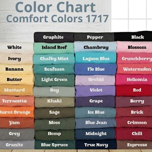 Op de afbeelding: Een Comfort Colors 1717 kleurenkaart met een raster van gevouwen t-shirts in diverse tinten. De tekst luidt Color Chart Comfort Colors 1717, met labels voor elke kleur, waaronder White, Ivory, Banana, Butter, Mustard, Terracotta, Burnt Orange, Yam, Grey, Granite, Graphite, Island Reef, Chalky Mint, Seafoam, Light Green, Bay, Khaki, Sage, Moss, Hemp, Blue Spruce, Pepper, Chambray, Lagoon Blue, Flo Blue, Orchid, Violet, Grape, Ice Blue, Blue Jean, Midnight, True Navy, Black, Blossom, Crunchberry, Watermelon, Heliconia, Red, Berry, Brick, Crimson, Chili en Espresso.