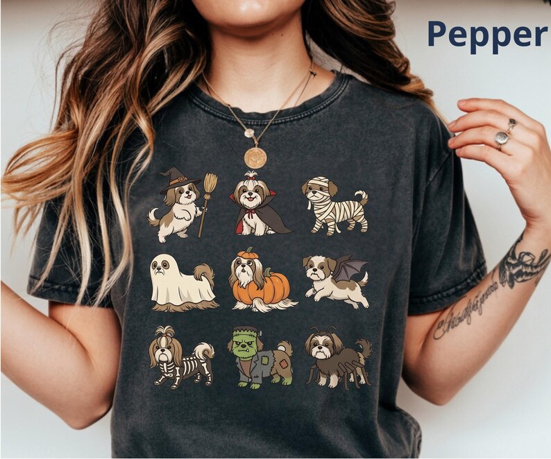 Op de afbeelding: Een antracietgrijs t-shirt met een grafische print van negen Shih Tzu honden in verschillende Halloween-kostuums, waaronder een heks, vampier, mummie, spook, pompoen, vleermuis, skelet, het monster van Frankenstein en een spin.