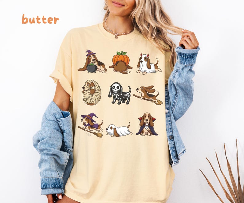 Pu&ograve; includere: Una t-shirt color burro con una stampa grafica di nove cani Basset Hound in vari costumi di Halloween, tra cui una strega, una zucca, un fantasma, una mummia, uno scheletro, un vampiro e cani su manici di scopa, con il testo butter.