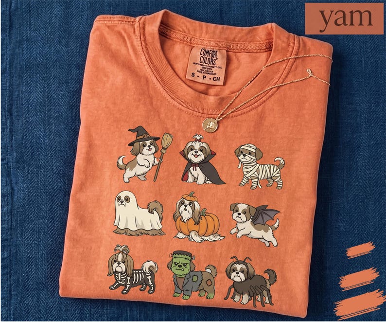 Op de afbeelding: Een oranje T-shirt met korte mouwen en een grafische print van negen Shih Tzu-honden in verschillende Halloween-kostuums, waaronder een heks, vampier, mummie, spook, pompoen, vleermuis, skelet, het monster van Frankenstein en een spin.