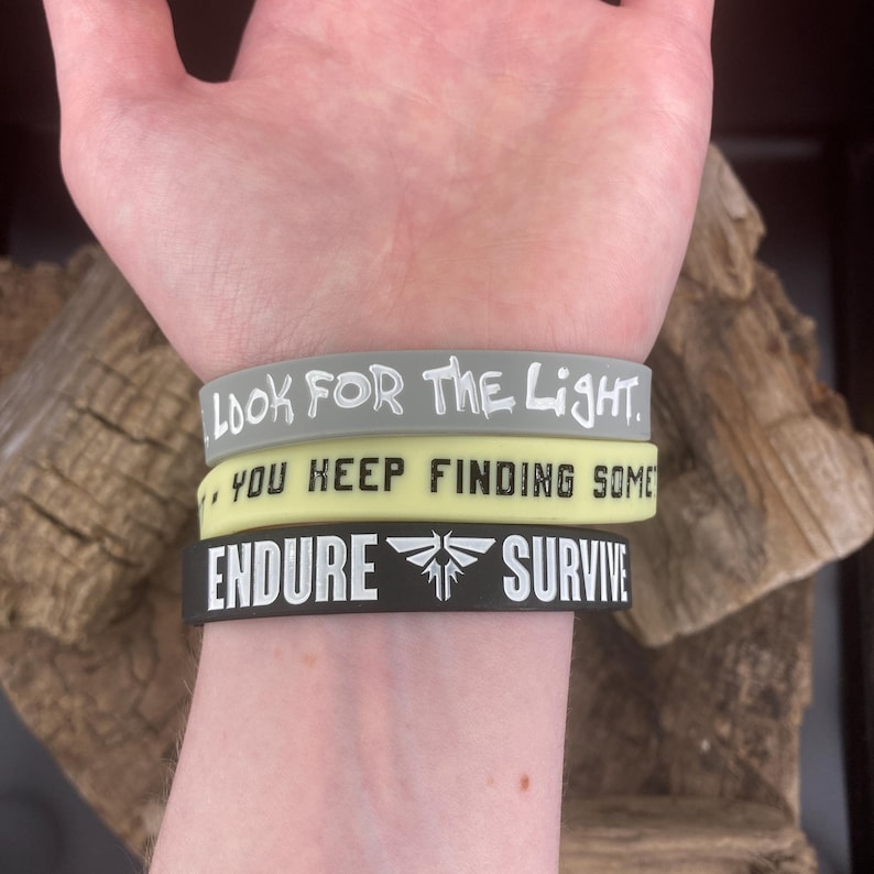 Pu&ograve; includere: Tre braccialetti in silicone con testo bianco. Il braccialetto superiore &egrave; grigio e dice "Cerca la luce." Il braccialetto intermedio &egrave; giallo e dice "Continui a trovarne." Il braccialetto inferiore &egrave; nero e dice "Resisti" e "Sopravvivi" con un simbolo di lucciola in mezzo.