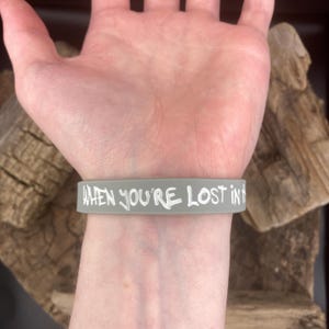 Pu&ograve; includere: Braccialetto in silicone grigio con il testo "WHEN YOU'RE LOST IN THE" in lettere bianche.