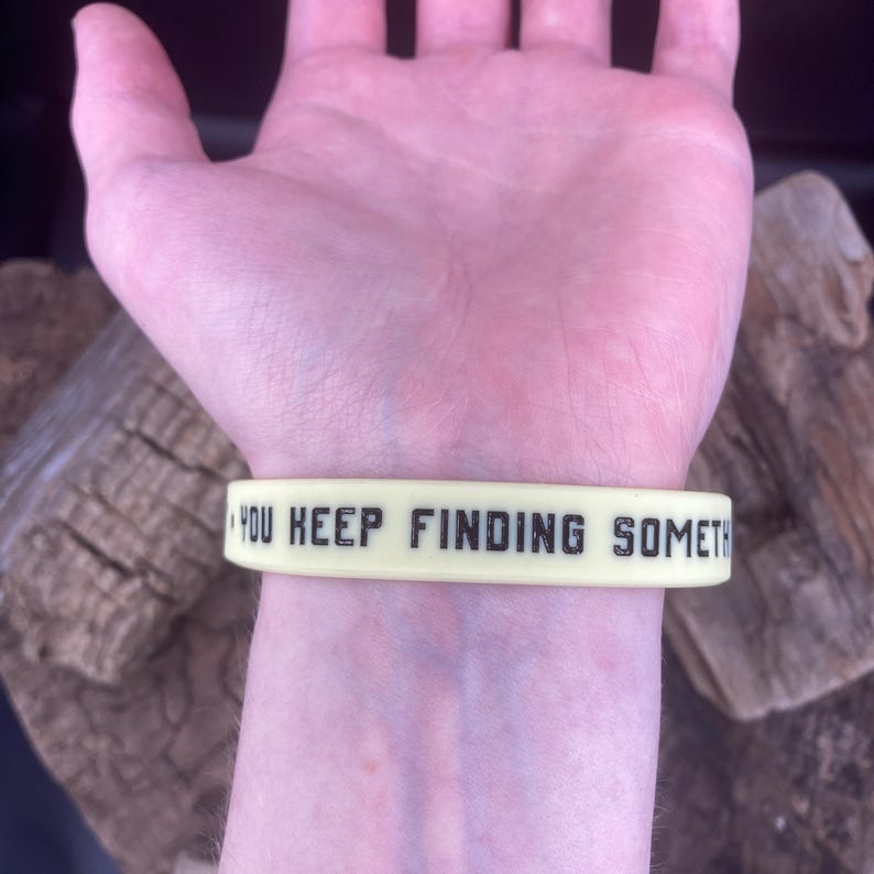 Pu&ograve; includere: Un braccialetto in silicone giallo con il testo "YOU KEEP FINDING SOMETHING" in lettere nere.
