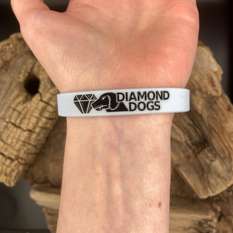 Puede incluir: Pulsera de silicona blanca con texto negro y una silueta de diamante y perro. El texto dice "DIAMOND DOGS".
