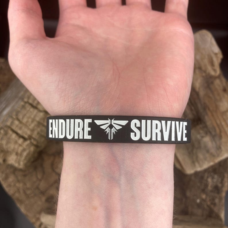 Pu&ograve; includere: Braccialetto in silicone nero con testo bianco che recita "ENDURE" e "SURVIVE" con un simbolo di lucciola tra le parole.