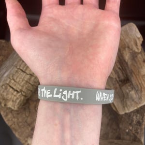 Pu&ograve; includere: Braccialetto in silicone grigio con testo bianco che recita "FOR THE LIGHT. WHEN YOU"