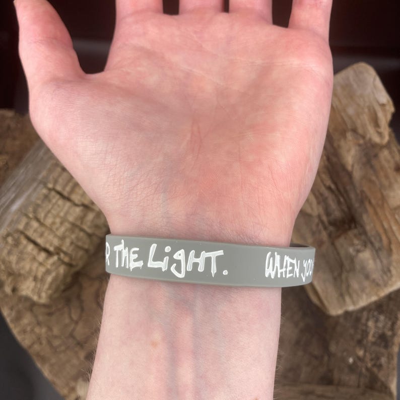Pu&ograve; includere: Braccialetto in silicone grigio con testo bianco che recita "FOR THE LIGHT. WHEN YOU"