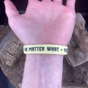 Pu&ograve; includere: Un braccialetto in silicone giallo con il testo "NO MATTER WHAT - YOU" stampato in nero.