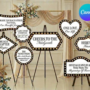 May include: A collection of white wedding signs with black borders and illuminated bulbs, featuring various romantic phrases like Cheers to the Newlyweds, One Love, One Life, and The Next Chapter Begins, displayed on black metal tripod easels.