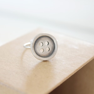 Pode incluir: Um anel de prata com um design de botão de quatro furos.