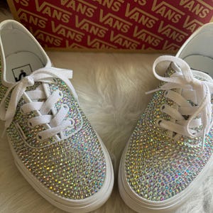 May include: A pair of white canvas low-top sneakers covered in iridescent rhinestones.