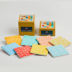 May include: Set of eight colourful ceramic coasters with geometric patterns. The coasters are packaged in two boxes with the text "Simple Design ceramic coasters".