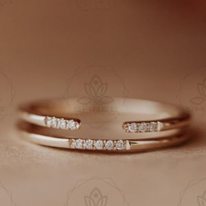 May include: A delicate gold ring with a thin band and a row of small diamonds set in the centre. The ring is designed to be worn as a double band, with the two bands overlapping.