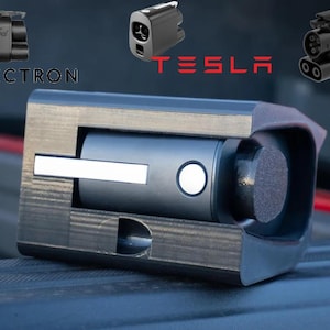 Op de afbeelding: Een zwarte adapter met een zilveren rand en een witte knop. De adapter is ontworpen om een ​​elektrisch voertuig aan een laadstation te verbinden. De adapter is gelabeld met "A2Z EV".