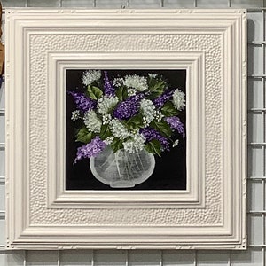 May include: A white frame with a textured surface surrounds a painting of a bouquet of purple and white flowers in a clear vase against a black background.