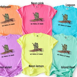 Pu&ograve; includere: Sei magliette a maniche corte nei colori melone neon, rosa neon, laguna, viola neon, limone neon e barriera corallina. Ogni maglietta presenta la grafica di una rana verde su una tavola da paddle con la scritta WE PADDLE AT DAWN in nero.