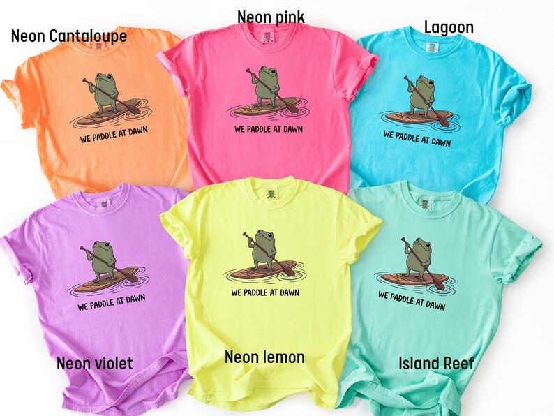Pu&ograve; includere: Sei magliette a maniche corte nei colori melone neon, rosa neon, laguna, viola neon, limone neon e barriera corallina. Ogni maglietta presenta la grafica di una rana verde su una tavola da paddle con la scritta WE PADDLE AT DAWN in nero.