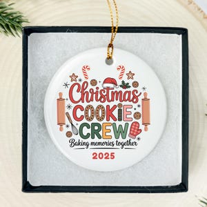 May include: A white ceramic Christmas ornament with the words "Christmas COOKIE CREW" in red and green, surrounded by festive baking-themed graphics. The text "Baking memories together 2025" is also included.
