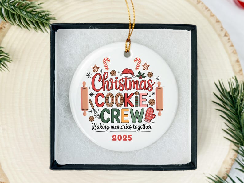 May include: A white ceramic Christmas ornament with the words "Christmas COOKIE CREW" in red and green, surrounded by festive baking-themed graphics. The text "Baking memories together 2025" is also included.
