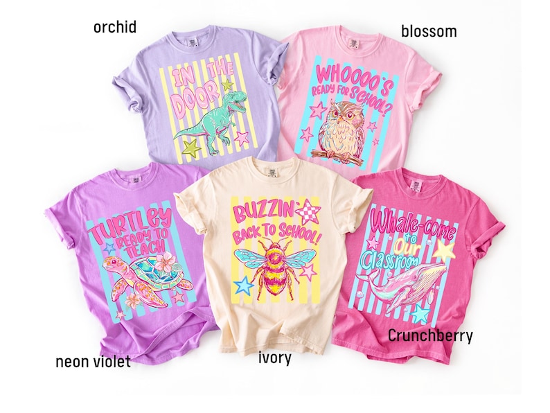 K&ouml;nnte beinhalten: F&uuml;nf kurz&auml;rmelige T-Shirts in den Farben Orchidee, Bl&uuml;te, Neonviolett, Elfenbein und Crunchberry. Jedes Shirt zeigt einen Grafikdruck mit Text: In the Door mit einem Dinosaurier, Whoooo's Ready for School mit einer Eule, Turtley Ready to Teach mit einer Schildkr&ouml;te, Buzzin Back to School mit einer Biene und Whale-come to Our Classroom mit einem Wal.