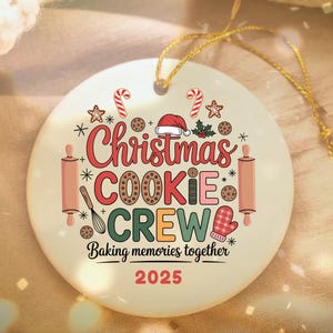 May include: A round, off-white Christmas ornament with the words "Christmas Cookie Crew" in red, green, and brown. The ornament features festive illustrations of candy canes, cookies, and a Santa hat. The text "Baking memories together 2025" is also included.