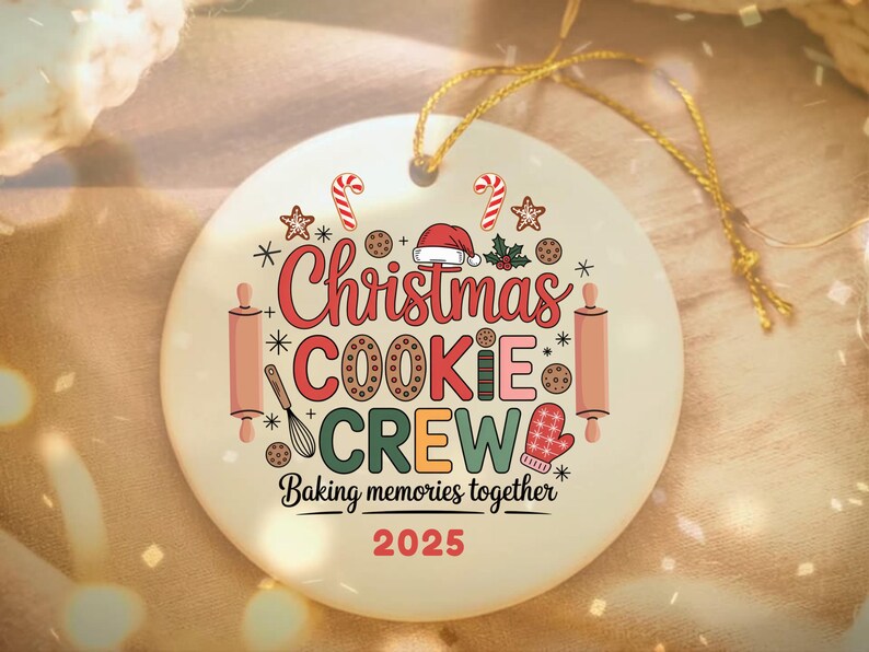 May include: A round, off-white Christmas ornament with the words "Christmas Cookie Crew" in red, green, and brown. The ornament features festive illustrations of candy canes, cookies, and a Santa hat. The text "Baking memories together 2025" is also included.