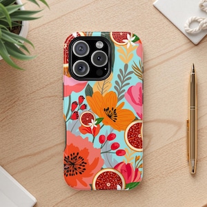 May include: A colorful phone case with a floral design featuring orange and pink flowers, red berries, and citrus fruit slices on a light blue background. The case is on a wooden surface with a gold pen and a small plant.