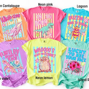 K&ouml;nnte beinhalten: Sechs kurz&auml;rmelige T-Shirts in Neon-Cantaloupe, Neon-Pink, Lagune, Neon-Violett, Neon-Zitrone und Inselriff. Jedes Shirt hat einen Hintergrund mit vertikalen Streifen und einen Grafikdruck mit Text: Whale-come to Our Classroom, In the Door, Buzzin Back to School, Turtley Ready to Teach, Whoooo's Ready for School und Lucky to See Your Face.