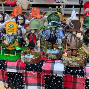 May include: A collection of handmade gnomes with various themes, including sports, fishing, and nature. The gnomes are displayed on a red and black plaid tablecloth with white stars.