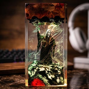 K&ouml;nnte beinhalten: Ein rechteckiges Kunstwerk aus Harz mit einer Scream-Figur. Die Figur ist schwarz und steht auf einem gr&uuml;nen und roten Sockel mit wirbelnden gelben und gr&uuml;nen Akzenten. Der obere Teil hat ein dunkelbraunes Holzmaserungsdesign.