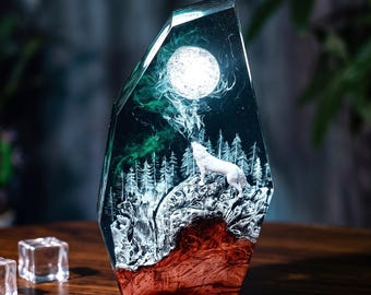 Puede incluir: Una escultura de resina con forma de prisma de cristal alto e irregular. En su interior, un lobo blanco se alza sobre una base texturizada de color marrón rojizo, aullando a una luna blanca brillante sobre un bosque de pinos.