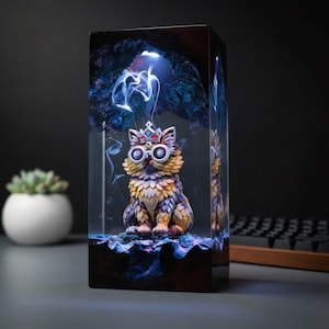 May include: A decorative resin sculpture of a cat wearing a crown and goggles, encased in a rectangular block. The cat is detailed with shades of yellow, orange, and purple. The block has a dark base and a lit, smoky top, creating a fantasy theme.