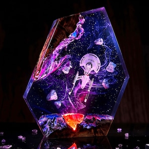 May include: A hexagonal resin sculpture featuring a miniature starship model suspended in a deep space scene with purple and blue nebula clouds, scattered white stars, and floating asteroids, anchored by a glowing orange base and dark wood.