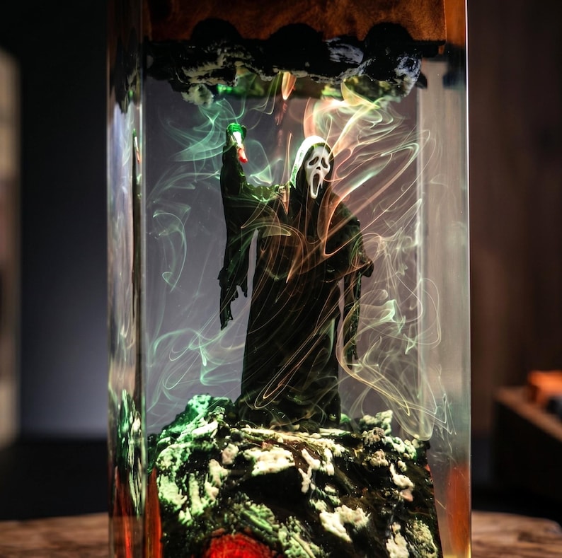 K&ouml;nnte beinhalten: Ein Kunstwerk aus Kunstharz mit einer Scream-Figur, die ein gr&uuml;nes Licht h&auml;lt. Die Figur ist in einem transparenten rechteckigen Block mit farbigen Wirbeln und einer felsigen Basis eingeschlossen. Die Oberseite hat dunkle, strukturierte Elemente.
