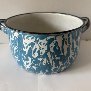 Könnte beinhalten: Eine weiße Emaille-Schüssel mit blauer Marmorierung und schwarzem Rand. Die Schüssel hat zwei schwarze Griffe.