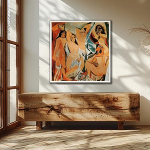 Puede incluir: Una pintura abstracta enmarcada que presenta figuras desnudas en tonos naranja, beige y azul. La obra de arte se exhibe en una pared blanca sobre un mueble de madera. La pintura tiene un borde blanco.