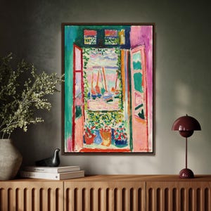 Könnte beinhalten: Gerahmtes abstraktes Gemälde, das ein Fenster mit Blick auf einen Hafen mit Segelbooten darstellt. Das Kunstwerk verwendet leuchtende Farben, darunter Rosa, Grün, Blau und Orange. Das Gemälde wird auf einem Holzschrank mit einer dekorativen Lampe und einer Vase in der Nähe ausgestellt.