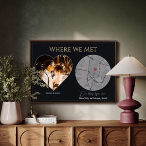 Puede incluir: Una impresión enmarcada en negro y dorado con el texto "WHERE WE MET". La impresión presenta una foto en forma de corazón y un mapa con un corazón rojo. El texto debajo dice "Sarah & John" y "Our story began here. New York, 14 February 2020."