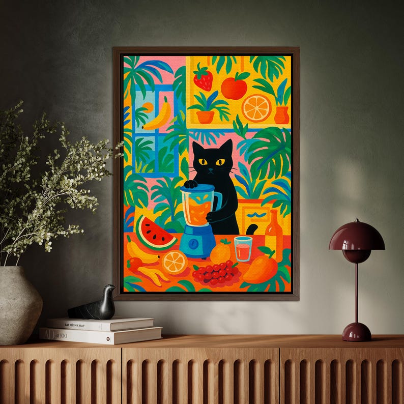 May include: A framed wall art print featuring a black cat standing at a table, blending fruit in a blue blender. The vibrant illustration includes a watermelon slice, bananas, oranges, grapes, a mango, and a glass of juice, all surrounded by lush green tropical foliage and a window.