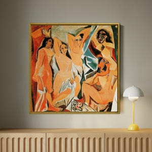 Puede incluir: Pintura abstracta enmarcada que presenta figuras desnudas en tonos naranja, beige y azul. La obra de arte tiene un marco dorado y se exhibe sobre un mueble de madera. Una l&aacute;mpara amarilla y blanca est&aacute; sobre el mueble.