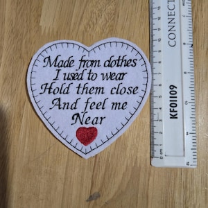 May include: White felt heart-shaped patch with a red embroidered heart and black embroidered text that reads "Made from clothes I used to wear Hold them close And feel me Near".