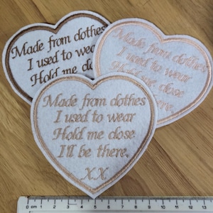 May include: Three white felt heart-shaped patches with brown embroidered text. The text reads: "Made from clothes I used to wear Hold me close" and "Made from clothes I used to wear Hold me close I'll be there. XX".