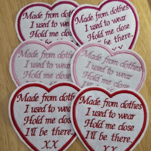 May include: Six white felt heart-shaped patches with red and pink stitching. The patches have the text "Made from clothes I used to wear Hold me close I'll be there. XX" embroidered on them.