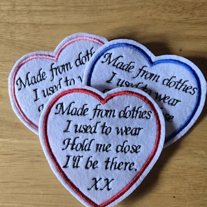 May include: Three heart-shaped patches with embroidered text. The patches are white with coloured borders in pink, blue, and red. The text reads "Made from clothes I used to wear. Hold me close, I'll be there. XX."