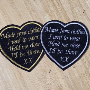 May include: Two heart-shaped embroidered patches. One has a black background with gold trim and text that reads "Made from clothes I used to wear Hold me close I'll be there. XX". The other has a black background with silver trim and similar text.