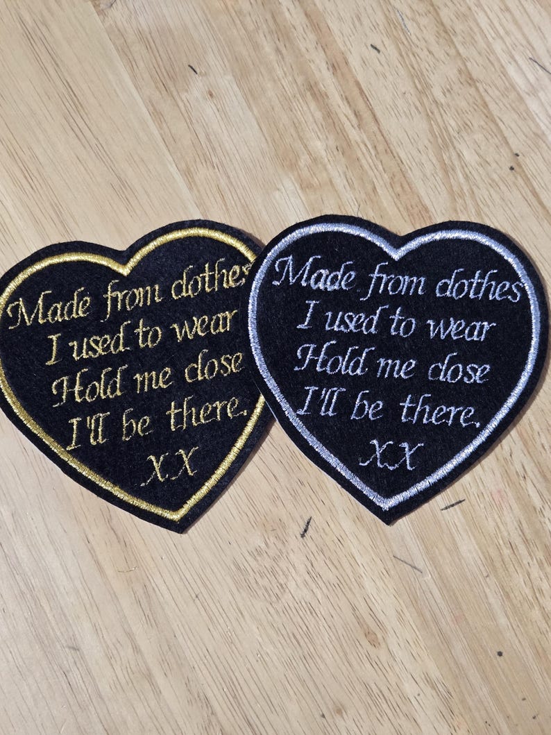 Pode incluir: Duas aplica&ccedil;&otilde;es bordadas em forma de cora&ccedil;&atilde;o. Uma tem fundo preto com contorno dourado e o texto "Made from clothes I used to wear Hold me close I'll be there. XX". A outra tem fundo preto com contorno prateado e texto semelhante.